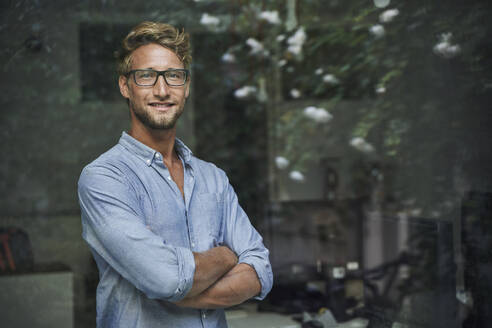 Portrait of casual young businessman behind windowpane in office - PNEF02085