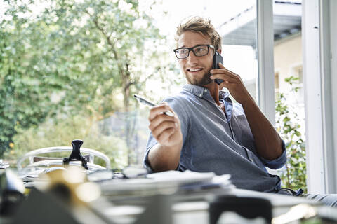 Lässiger junger Geschäftsmann am Telefon am Schreibtisch im Büro, lizenzfreies Stockfoto