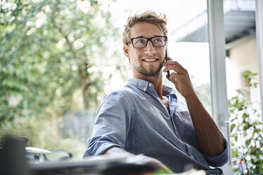 Casual young businessman on the phone at desk in office - PNEF02096