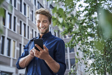 Happy young businessman using mobile phone in the city - PNEF02113