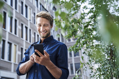 Smiling young businessman using mobile phone in the city - PNEF02114