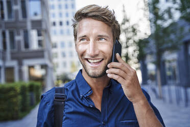 Portrait of happy young businessman on the phone in the city - PNEF02115