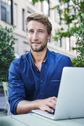 Porträt eines jungen Geschäftsmannes mit Laptop in einem Straßencafé in der Stadt - PNEF02117