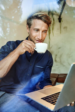 Junger Geschäftsmann trinkt Kaffee und benutzt einen Laptop in einem Café, lizenzfreies Stockfoto