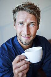 Portrait of young man holding cup of coffee - PNEF02147