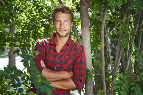 Portrait of confident young man wearing checkered shirt leaning against a tree stock photo