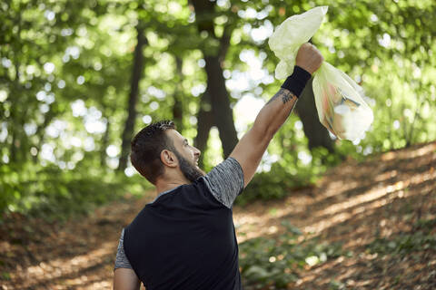 Sportlicher Mann mit Müllsack im Wald, lizenzfreies Stockfoto