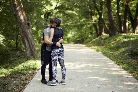 Sportliches Paar, das sich auf einem Waldweg umarmt, lizenzfreies Stockfoto