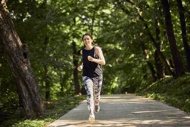 Sportliche junge Frau läuft auf einem Waldweg - ZEDF02629