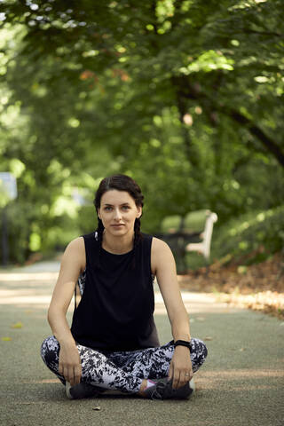 Porträt einer sportlichen jungen Frau, die auf einem Waldweg sitzt, lizenzfreies Stockfoto