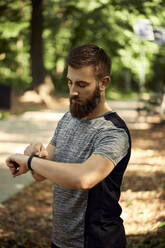 Sportlicher Mann im Wald überprüft seine Smartwatch - ZEDF02639