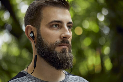 Portrait of sporty man with earphones in forest - ZEDF02641