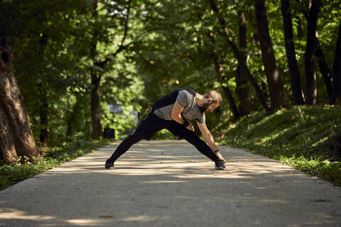 Sportlicher Mann beim Stretching auf einem Waldweg, lizenzfreies Stockfoto