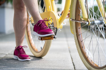 Der Fuß einer Frau tritt auf das Pedal ihres gelben Fahrrads, um sich auf die Fahrt vorzubereiten - CAVF64696