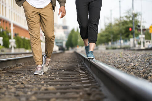 Junges Paar, das von der Taille abwärts auf den Bahngleisen in einer Stadt spazieren geht - CAVF64792