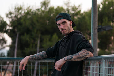 Man with tattoos in his arms is posing in a park - CAVF64794