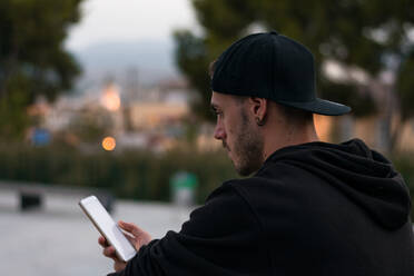Mann mit Mütze schaut auf sein Smartphone, im Hintergrund sind die Lichter der Stadt zu sehen - CAVF64795