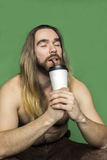 Porträt eines bärtigen Mannes, der ein Getränk vor einem grünen Hintergrund genießt - VGF00311