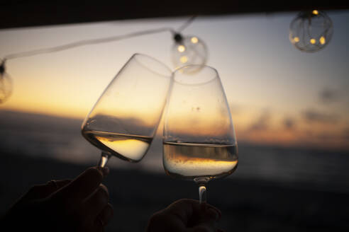 Frau hält zwei Gläser Weißwein in einem Van bei Sonnenuntergang - NAF00140