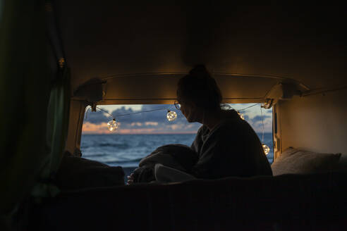Frau in einem Lieferwagen schaut seitwärts in den Sonnenuntergang - NAF00145
