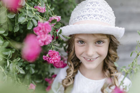 Porträt eines lächelnden Mädchens am Rosenstrauch, lizenzfreies Stockfoto