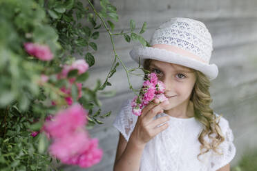 Porträt eines Mädchens am Rosenstrauch, das an der Blüte riecht - STBF00429
