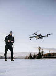 Ein Mann fliegt im Winter bei Sonnenuntergang eine Drohne. - CAVF64824