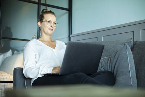 Frau arbeitet im Hotelzimmer, sitzt auf der Couch, lizenzfreies Stockfoto