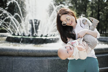 Mother playing with her baby boy near a fountain - EYAF00541