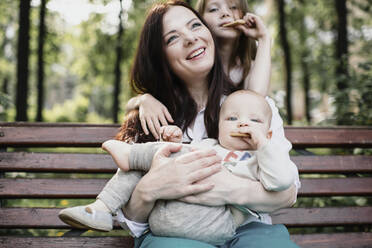 Smiling mother with her two kids eating cookies in the park - EYAF00542