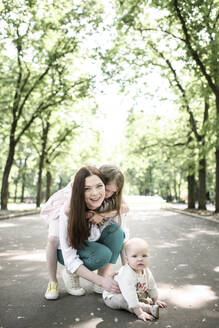 Lächelnde Mutter mit ihren beiden Kindern im Park - EYAF00543