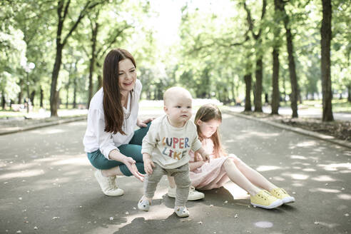 Lächelnde Mutter mit ihren beiden Kindern im Park - EYAF00544