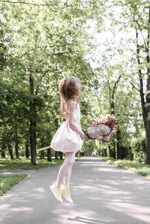 Niedliches kleines Mädchen in einem Park, das mit ihrem Steckenpferd springt - EYAF00556