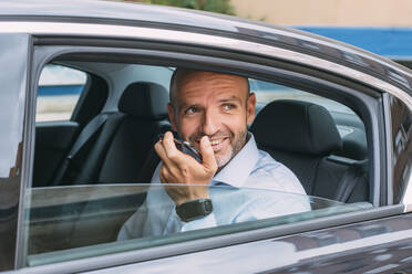 Geschäftsmann auf dem Rücksitz eines Autos, der sein Smartphone benutzt und sich umschaut - CJMF00083