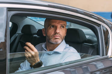 Geschäftsmann auf dem Rücksitz eines Autos, der sein Smartphone benutzt und sich umschaut - CJMF00084