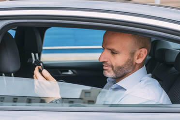 Geschäftsmann sitzt auf der Rückbank des Autos und benutzt ein Smartphone - CJMF00085