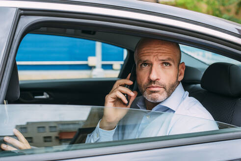 Geschäftsmann auf dem Rücksitz eines Autos, der sein Smartphone benutzt und sich umschaut - CJMF00086