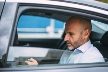 Geschäftsmann sitzt auf der Rückbank des Autos und benutzt ein Smartphone - CJMF00087