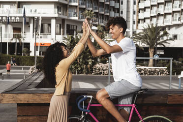 Young couple with bicycle, high-fiving in the city - RCPF00018