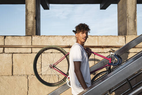 Junger Mann auf der Treppe, der ein Fahrrad auf den Schultern trägt - RCPF00021