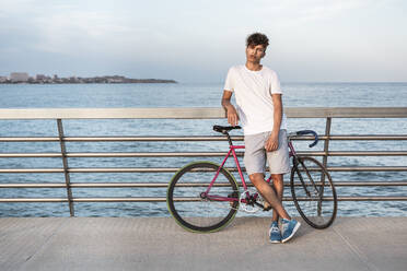 Junger Mann mit Fahrrad, stehend auf Brücke am Meer - RCPF00035