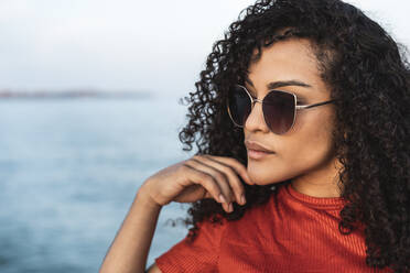 Beautiful woman, wearing sunglasses, standing at the sea, looking away - RCPF00042