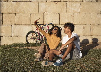 Young couple taking selfies with smartphone, sitting in front of wall - RCPF00057