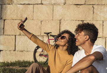 Junges Paar macht Selfies mit Smartphone, sitzt vor einer Wand - RCPF00058