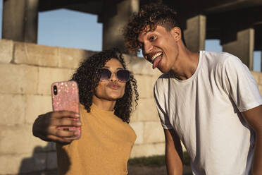 Junges Paar macht Selfies mit Smartphone, sitzt vor einer Wand - RCPF00060