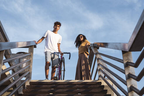 Junges Paar mit Fahrrad, stehend auf einer Treppe - RCPF00063