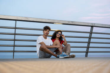 Junges Paar sitzt auf einer Brücke am Meer - RCPF00079