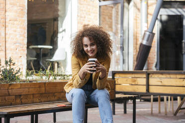 Porträt eines lächelnden Teenagers auf einer Bank mit einem Kaffee zum Mitnehmen - VPIF01536