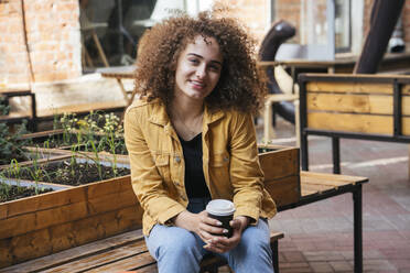 Porträt eines lächelnden Teenagers auf einer Bank mit einem Kaffee zum Mitnehmen - VPIF01537