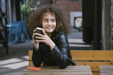 Porträt eines lächelnden Teenagers auf einer Bank mit einem Kaffee zum Mitnehmen, lizenzfreies Stockfoto